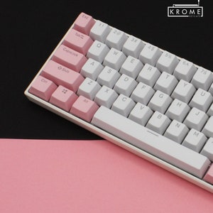 May include: A white and pink mechanical keyboard with a white space bar and pink keys for the control, tab, caps lock, shift, and alt keys. The keyboard has a black background.