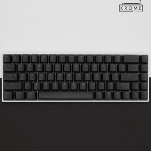 May include: A black mechanical keyboard with white keycaps and a white frame. The keyboard has a standard layout with function keys, number keys, and arrow keys. The keyboard is on a white surface.