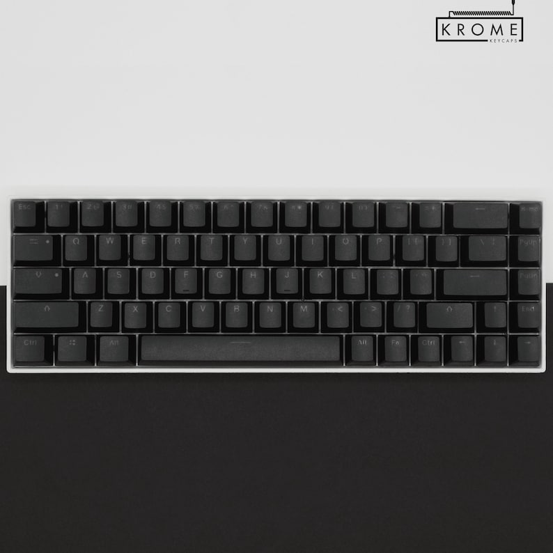 May include: A black mechanical keyboard with white keycaps and a white frame. The keyboard has a standard layout with function keys, number keys, and arrow keys. The keyboard is on a white surface.
