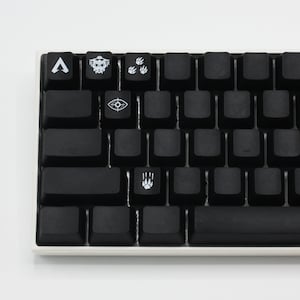 Pode incluir: Um teclado mec&acirc;nico preto com teclas personalizadas que apresentam s&iacute;mbolos do videogame Apex Legends. As teclas incluem um s&iacute;mbolo para o personagem Bloodhound, um s&iacute;mbolo para o personagem Pathfinder, um s&iacute;mbolo para o personagem Octane e um s&iacute;mbolo para o personagem Wraith.