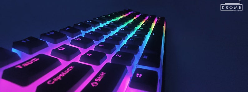 Op de afbeelding: Een wit mechanisch toetsenbord met zwarte toetsen en regenboogkleurige LED-achtergrondverlichting. Het toetsenbord is schuin geplaatst en de toetsen zijn gelabeld met letters en cijfers.