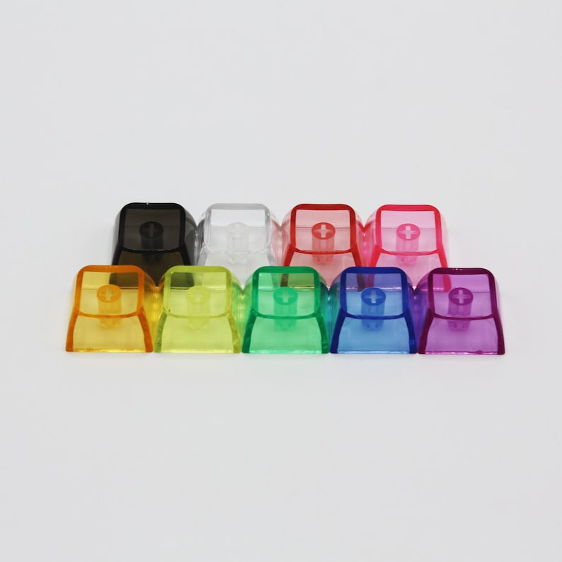 May include: Ten transparent keycaps in various colours, including yellow, green, blue, purple, red, and clear. The keycaps are arranged in a row, with the black keycap at the left end.