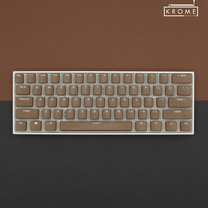 May include: A compact, white-framed keyboard with brown keycaps. The keys are arranged in a standard QWERTY layout. The keyboard has the brand name "KROME KEYCAPS" in the upper right corner. The background is a combination of brown and black.