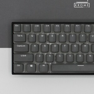 May include: A black keyboard with clear keycaps and white lettering. The keyboard has a standard layout with function keys, number keys, and letter keys. The keyboard also has a Caps Lock key, a Shift key, a Ctrl key, and an Alt key.