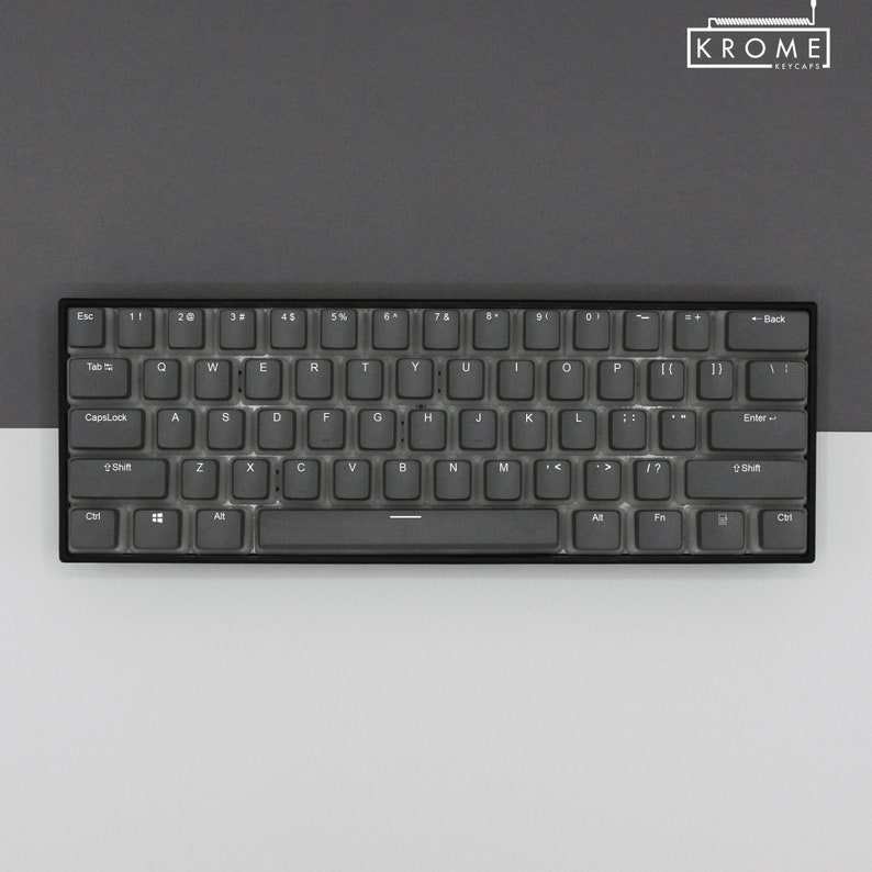 May include: A black and gray mechanical keyboard with a gray keycap set. The keyboard has a standard layout with function keys, arrow keys, and a number pad. The keys are labeled with white lettering. The keyboard is on a gray surface.