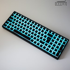 Puede incluir: Teclado mecánico negro con teclas blancas y retroiluminación azul. El teclado tiene un diseño compacto con un conjunto completo de teclas, incluidas las teclas de función y un teclado numérico. La marca "KROME KEYCAPS" está en la esquina superior derecha.
