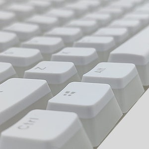Op de afbeelding: Wit mechanisch toetsenbord met toetsen die zijn gelabeld met letters en symbolen. Het toetsenbord is schuin van onder links naar boven rechts.