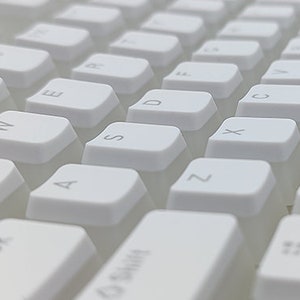 Op de afbeelding: Wit mechanisch toetsenbord met lege toetsen. Het toetsenbord heeft een standaard lay-out met functietoetsen, cijfertoetsen en lettertoetsen. Het toetsenbord is gemaakt van wit plastic en heeft een minimalistisch ontwerp.