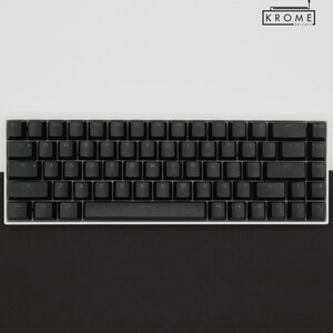 May include: A black mechanical keyboard with white keycaps and a white frame. The keyboard has a standard layout with function keys, number keys, and arrow keys. The keyboard is on a white surface.