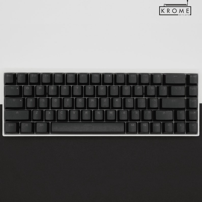 May include: A black mechanical keyboard with white keycaps and a white frame. The keyboard has a standard layout with function keys, number keys, and arrow keys. The keyboard is on a white surface.
