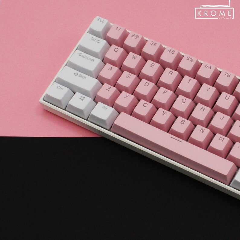 May include: A white and pink mechanical keyboard with a pink space bar and keycaps. The keys are labeled with the standard alphabet and number keys. The keyboard is on a pink surface.