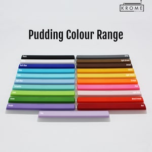 May include: A collection of colorful keycaps arranged in rows, showcasing a wide range of hues from black and white to vibrant shades of blue, green, and red. The text "Pudding Colour Range" is displayed above the keycaps, with the brand logo in the top right corner.