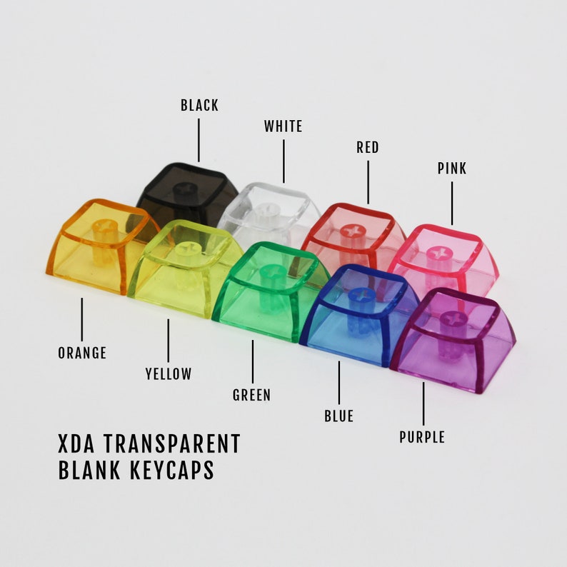 May include: A set of ten blank XDA profile keycaps in various transparent colours, including black, white, red, pink, orange, yellow, green, blue, and purple. The keycaps are arranged in a row from left to right, with the colours corresponding to the labels above them. The text "XDA TRANSPARENT BLANK KEYCAPS" is printed below the keycaps.