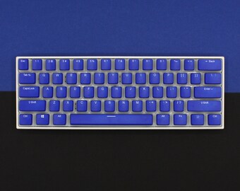 Könnte beinhalten: Eine kompakte, mechanische Tastatur mit blauen Tastenkappen und einem weißen Rahmen. Die Tasten sind in einem Standard-QWERTZ-Layout angeordnet. Der obere Hintergrund ist blau und der untere ist schwarz. Der Markenname "KROME KEYCAPS" steht oben rechts.