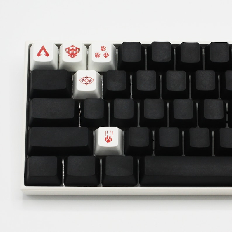 Peut inclure: Un clavier m&eacute;canique blanc avec des touches noires et cinq touches personnalis&eacute;es. Les touches ont des symboles rouges, dont un triangle, un vaisseau spatial, des empreintes de pattes, un &oelig;il et une empreinte de patte.