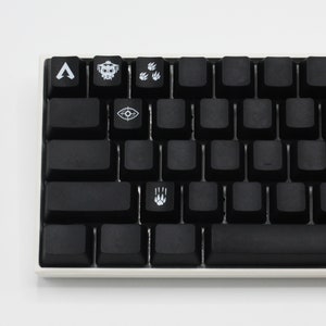 May include: A black mechanical keyboard with custom keycaps featuring symbols from the video game Apex Legends. The keycaps include a symbol for the character Bloodhound, a symbol for the character Pathfinder, a symbol for the character Octane, and a symbol for the character Wraith.
