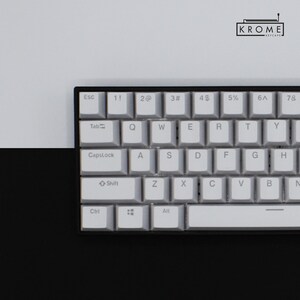 May include: A white mechanical keyboard with black keycaps and a black frame. The keys have white lettering and symbols. The keyboard has a row of function keys at the top, a row of number keys, a row of letter keys, and a row of modifier keys. The keyboard also has a space bar, a backspace key, and an enter key.