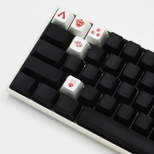 May include: A white mechanical keyboard with black keycaps and red and white keycaps with symbols. The symbols include a triangle, a skull, paw prints, and an eye.
