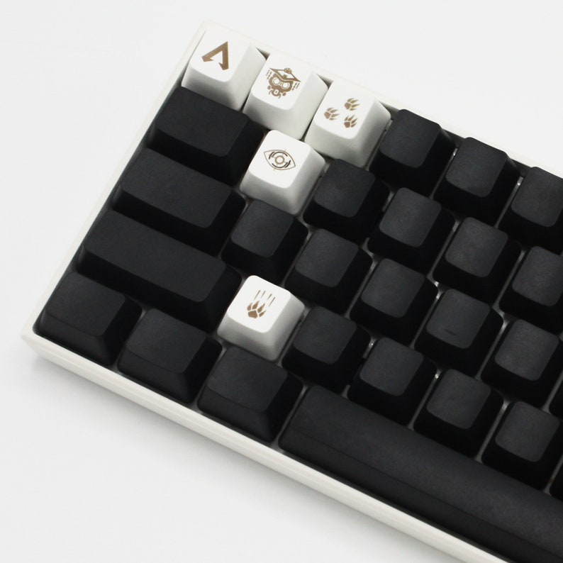 May include: A black mechanical keyboard with white keycaps featuring various symbols, including a triangle, an eye, and paw prints. The keyboard has a black space bar and a white frame.