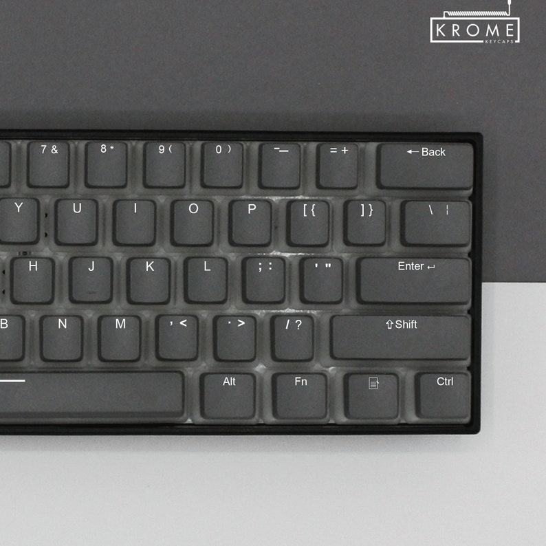 May include: A black mechanical keyboard with a gray keycap set. The keys are labeled with standard keyboard characters and symbols. The keyboard has a black frame and a black space bar.