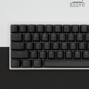 May include: A black mechanical keyboard with white keycaps and a white frame. The keys are labeled with the standard QWERTY layout. The keyboard has a space bar, a backspace key, an enter key, and a shift key. The keyboard is on a black surface.