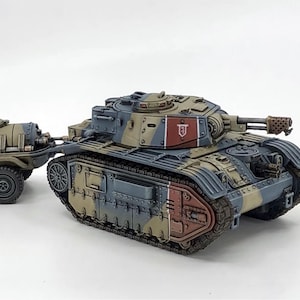 May include: A painted miniature tank model featuring a camouflage pattern of tan, blue-gray, and red panels. The tank has a rotating turret with a cannon, a front-mounted machine gun, and a two-wheeled supply trailer attached to the rear.