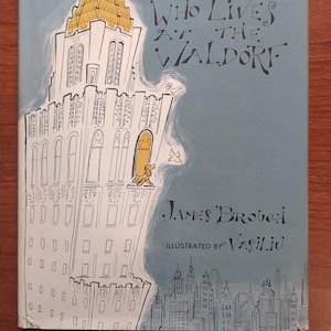 May include: Vintage book cover titled "The Dog Who Lives at the Waldorf." The cover features an illustration of a tall building with a gold-colored top and a dog figure in a window. The title and author's name are in black text against a light blue background.