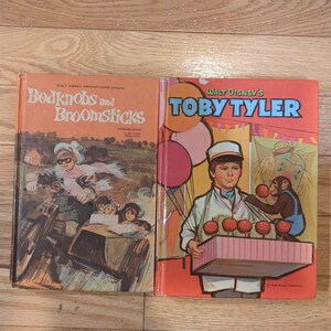 May include: Two vintage Walt Disney books: "Bedknobs and Broomsticks" and "Toby Tyler." The "Bedknobs" cover features a motorcycle scene, while "Toby Tyler" shows a boy with a tray of treats and a monkey. Both books have orange and red covers.