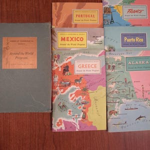 May include: A collection of vintage travel books from the American Geographical Society's "Around the World Program." Titles include Portugal, Mexico, Greece, France, Puerto Rico, and Alaska. The books feature colorful illustrations and maps.