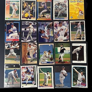 May include: A collection of baseball trading cards featuring Greg Maddux in various poses. The cards display action shots of Maddux pitching and include team logos and the text "Greg Maddux". The cards are in protective sleeves.