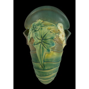 May include: A green and yellow ceramic wall vase with a floral design. The vase has a unique shape and is decorated with leaves and flowers.