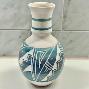 May include: A white ceramic vase with a teal blue geometric design. The vase has a narrow neck and a rounded body.