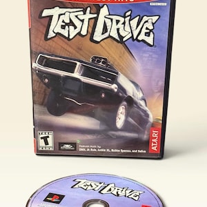 Può includere: Una custodia e un disco del videogioco PlayStation 2 Greatest Hits per Test Drive. La copertina presenta un'auto sportiva nera, il titolo Test Drive e i loghi PlayStation 2, la classificazione ESRB Teen e Atari. Il disco riporta gli stessi elementi.
