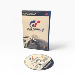 Puede incluir: Una caja de videojuego de PlayStation 2 y un disco para Gran Turismo 4. La caja presenta una portada blanca con el título del juego, un gráfico de coche y un símbolo de clasificación E. El disco circular muestra el logo y los iconos.