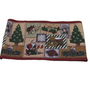 May include: A red, beige, and green Christmas-themed table runner with a patchwork design. The runner features images of Santa Claus, a teddy bear, a Christmas tree, a drum, a snowflake, and a candy cane.
