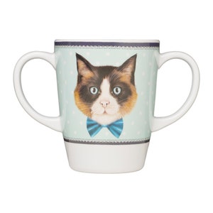 May include: A white ceramic mug with two handles features a colourful cat wearing a blue bow tie on a light blue background with white polka dots.