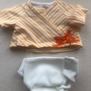 May include: A yellow and white striped shirt with orange ribbon detail and a white diaper.