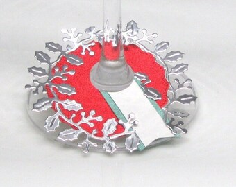 May include: Silver holly leaf design wine glass charm with a red and green tag for a name.