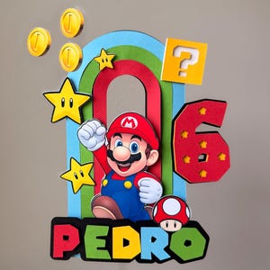 May include: A multi-layered cake topper featuring a cartoon character in a red hat and blue overalls, a rainbow arch, yellow stars, gold coins, a yellow question block, a red mushroom, and the number 6, with the name PEDRO in colorful letters.