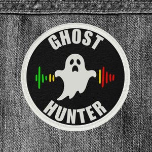 May include: A round black patch with the words "GHOST HUNTER" in white. A white ghost graphic is in the center, with green, yellow, and red sound wave graphics on either side. The patch has a white border.