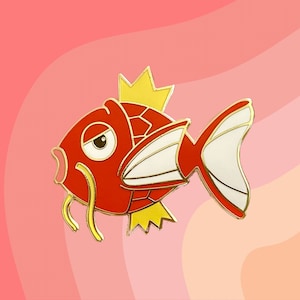 May include: A red and gold enamel pin of a cartoon fish with a crown on its head. The fish has a grumpy expression and a long, thin, yellow antenna.
