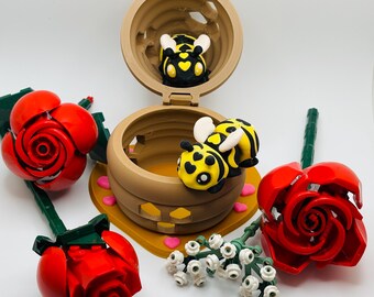 May include: A set of three red roses made of Lego bricks, a beehive with a bee inside, and a bee with black and yellow stripes flying out of the hive. The beehive is made of brown Lego bricks and has a pink heart design on the side.