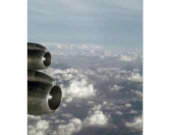 May include: A close-up of two silver airplane engine nacelles against a backdrop of white clouds. The engines are visible from the side, showing the intake and exhaust.
