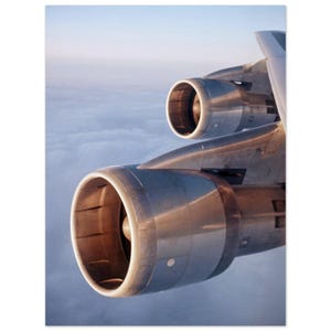 May include: A close-up of two large, silver aircraft engines against a cloudy sky. The engines are partially visible, with the front of the engines facing the viewer.