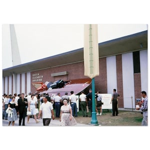 May include: A red and white speedboat on display at the Queen Elizabeth Building. The boat is tilted upwards and surrounded by people.