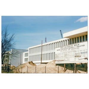 以下が含まれることがあります： 青い空を背景に、建設中の近代的な建物の写真。白い建物には一連の縦型の窓があります。建物の前にはテキストの看板があります。建設資材とクレーンも表示されています。