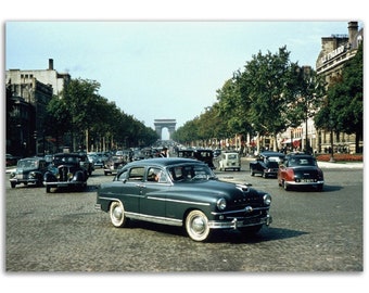 Op de afbeelding: Een vintage donkergroene auto rijdt over een straat in Parijs, Frankrijk. De Arc de Triomphe is in de verte zichtbaar.