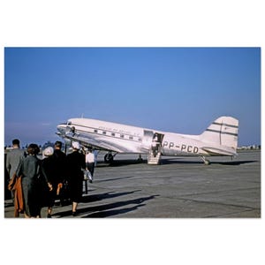 May include: A silver and white airplane with the text "Panair do Brasil S.A." and "PP-PCD" on the side. People are walking towards the airplane on a tarmac.