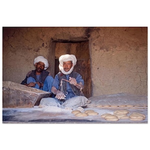 Peut inclure: Deux personnes portant des turbans blancs et des vêtements bleus préparent de la pâte dans une pièce rustique aux murs de terre. Une personne tient une petite balance à main au-dessus d'une surface couverte de farine et de boules de pâte.