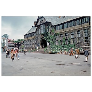 May include: A large stone building with a tiled roof and many windows. The building has a large entrance with steps leading up to it. There are people walking in front of the building.